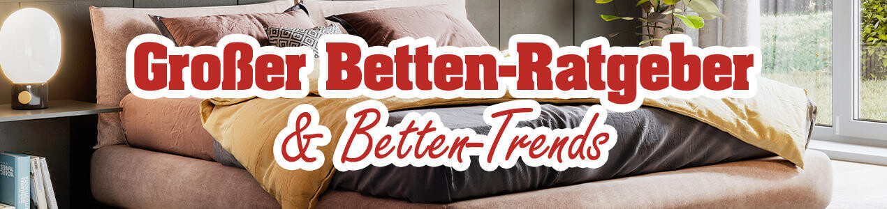 Ein modernes Bett mit einer beige-gelben Decke und einem grauen Bettlaken. Im Hintergrund große Fenster mit Tageslicht.